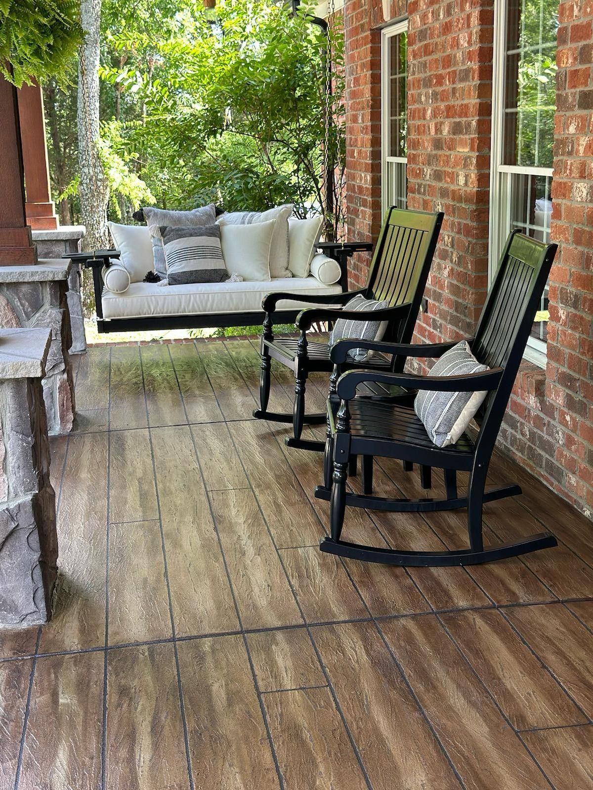 Covered brick porch with black rocking chairs, a white sofa, and weathered wooden floorboards