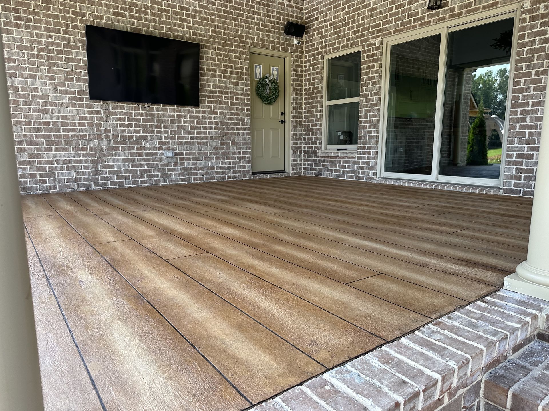 Covered brick patio with wood-look floor, white columns, and sliding glass doors.