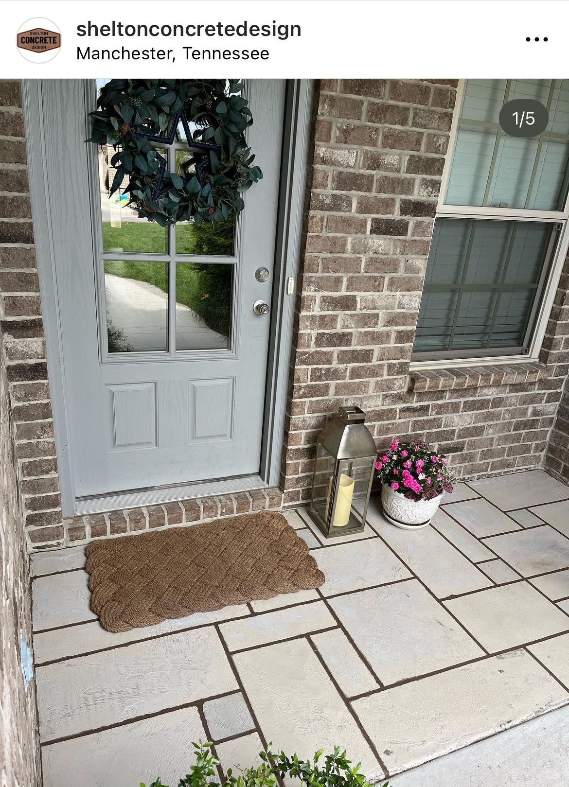 Front porch with gray front door, brick wall, paver walkway, doormat, lantern, and potted flowers