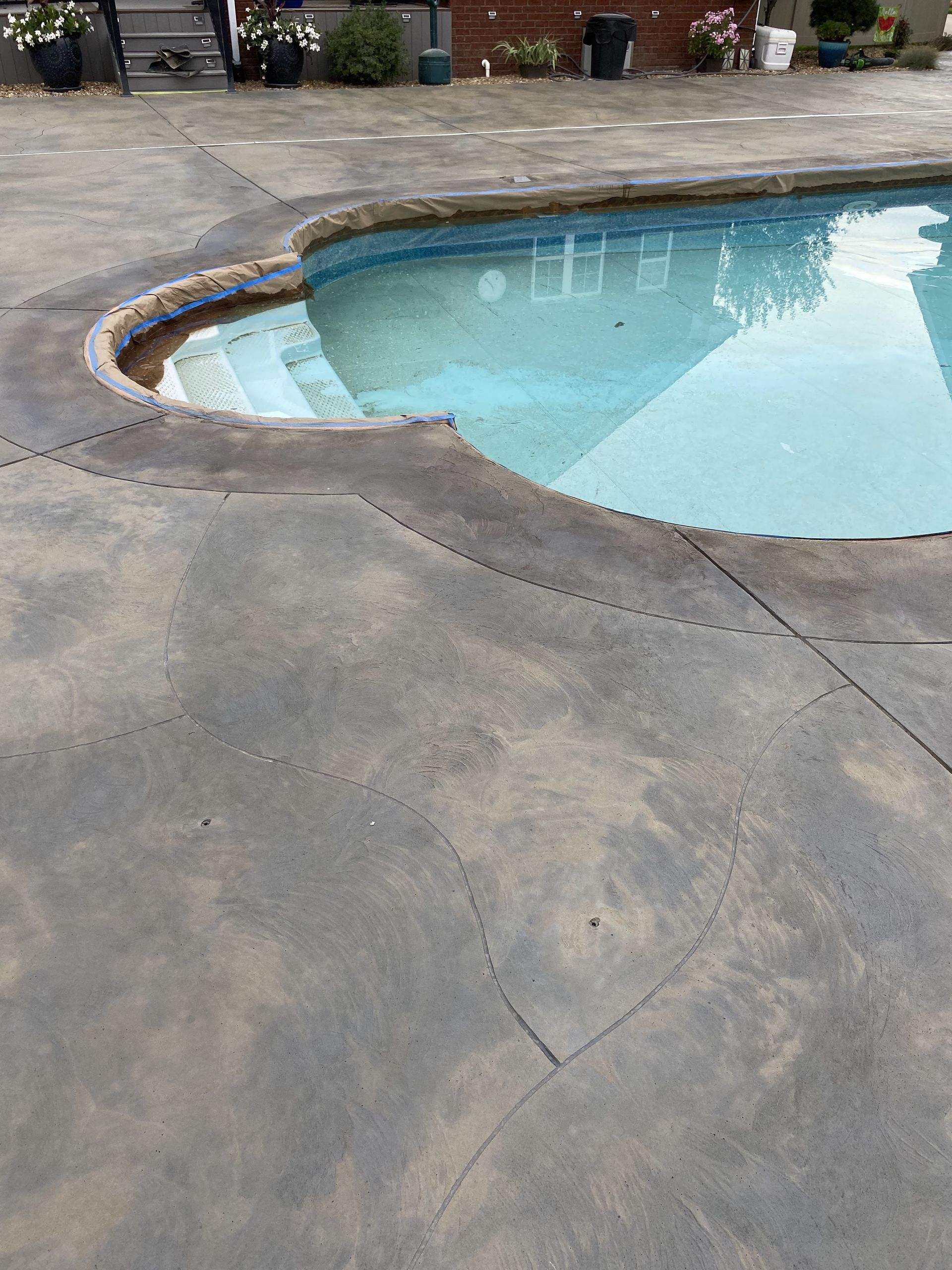 Curved backyard swimming pool with blue water beside a cracked concrete patio