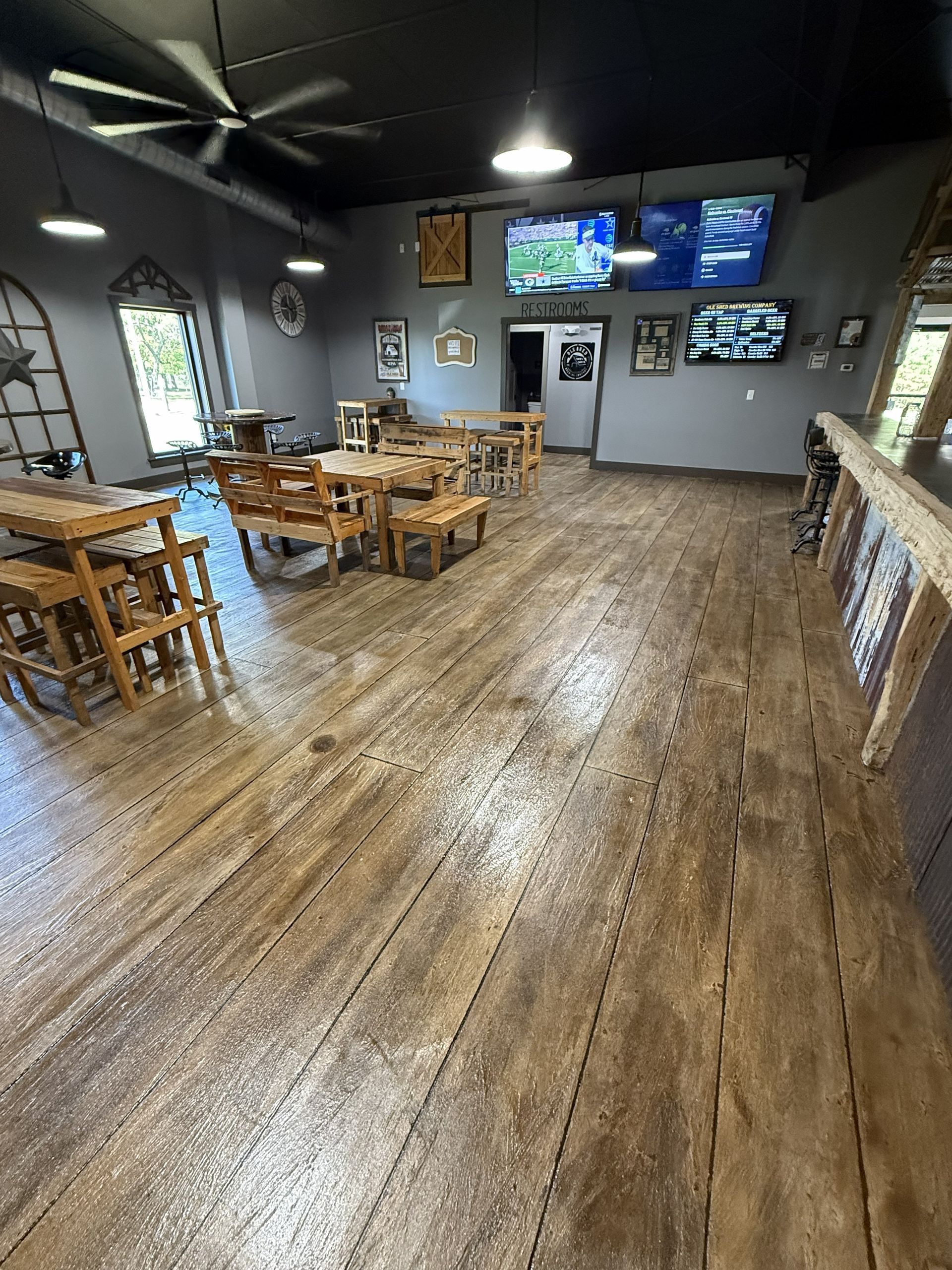 Empty rustic restaurant dining room with wooden tables, chairs, and wall-mounted TVs.