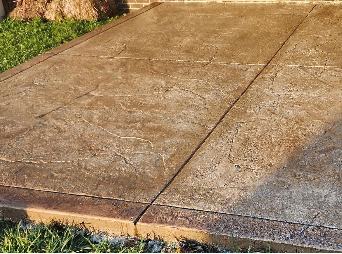 Concrete sidewalk with visible cracks and wet patches near grass and a stone edge