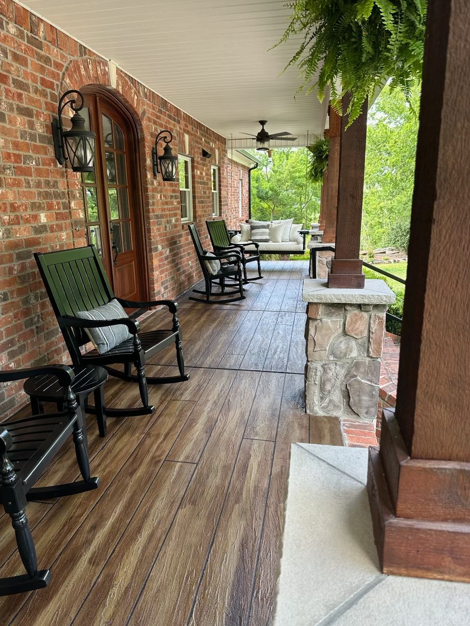 Brick porch with rocking chairs, wooden floor, and ceiling fan overlooking a green yard