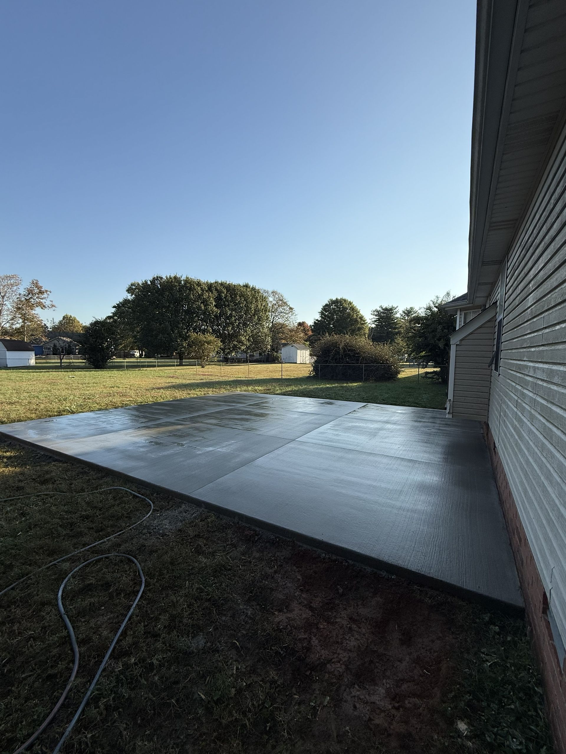 Concrete patio beside house and grassy yard under a clear blue sky.