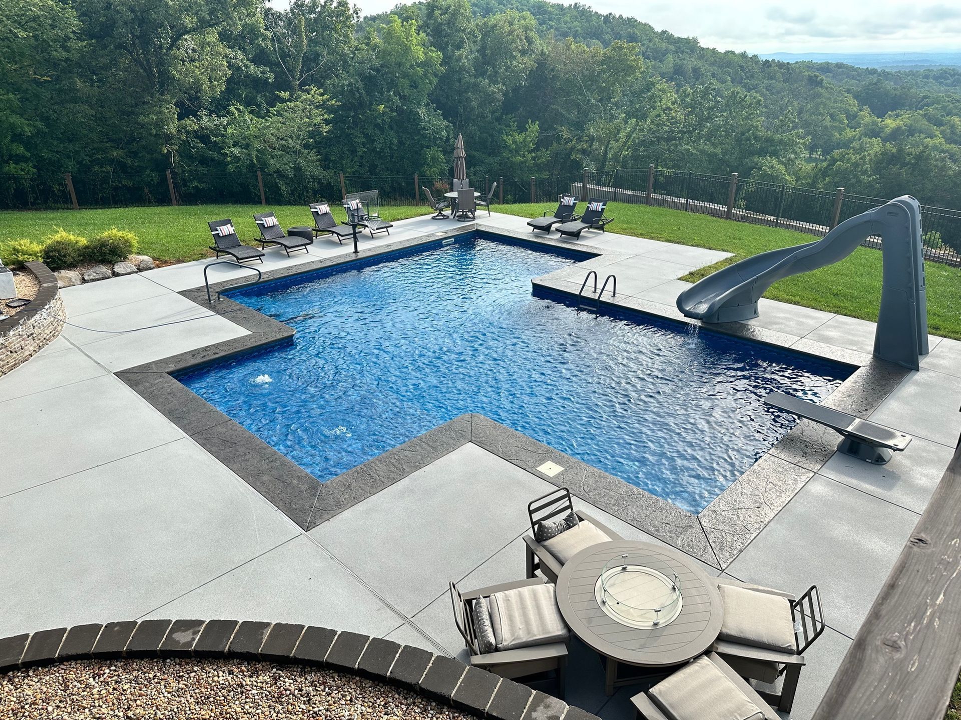 Backyard pool with blue water, lounge chairs, and a waterslide beside a landscaped patio