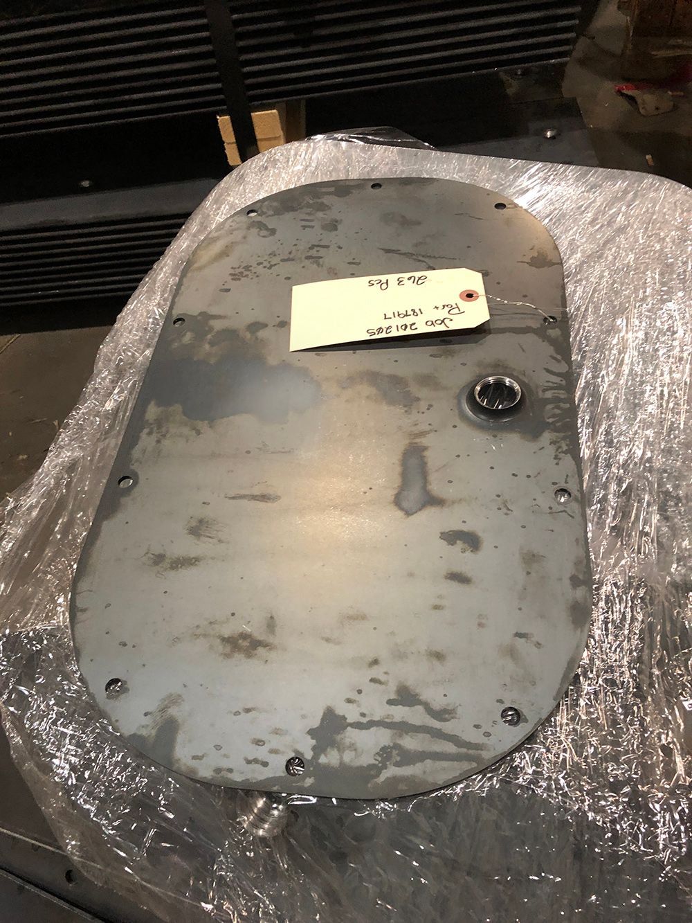 A piece of metal with a tag on it is wrapped in plastic.