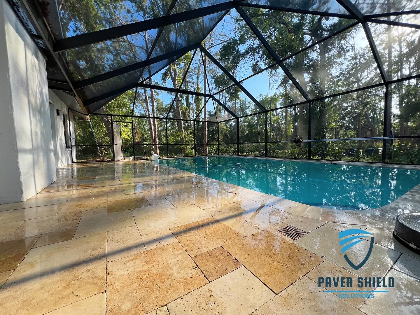 Screened-in pool patio with wet tile floor and blue water under bright sunlight