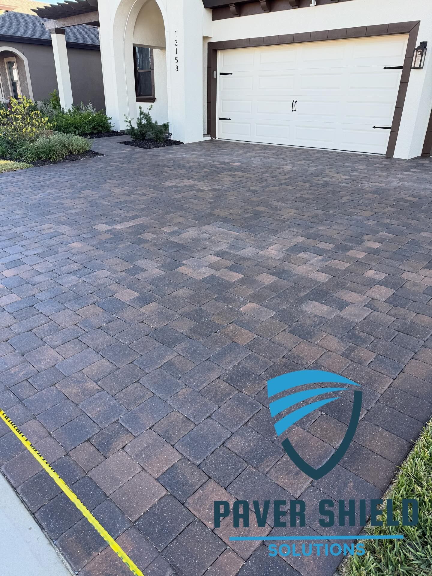 Brick paver driveway in front of a white garage and entryway with a yellow measuring tape at the lower left.