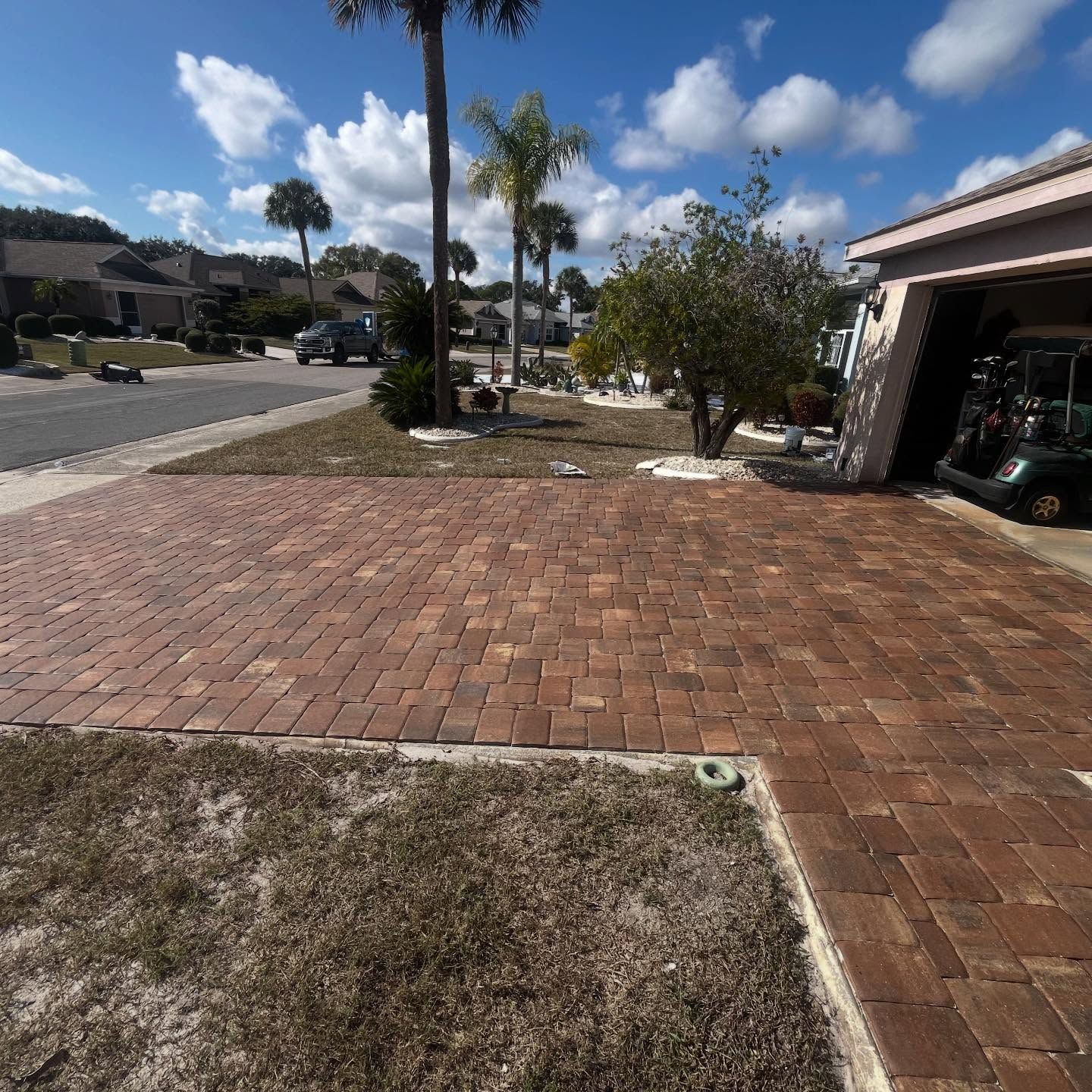 Brick-paved driveway and front yard beside a house under a sunny blue sky