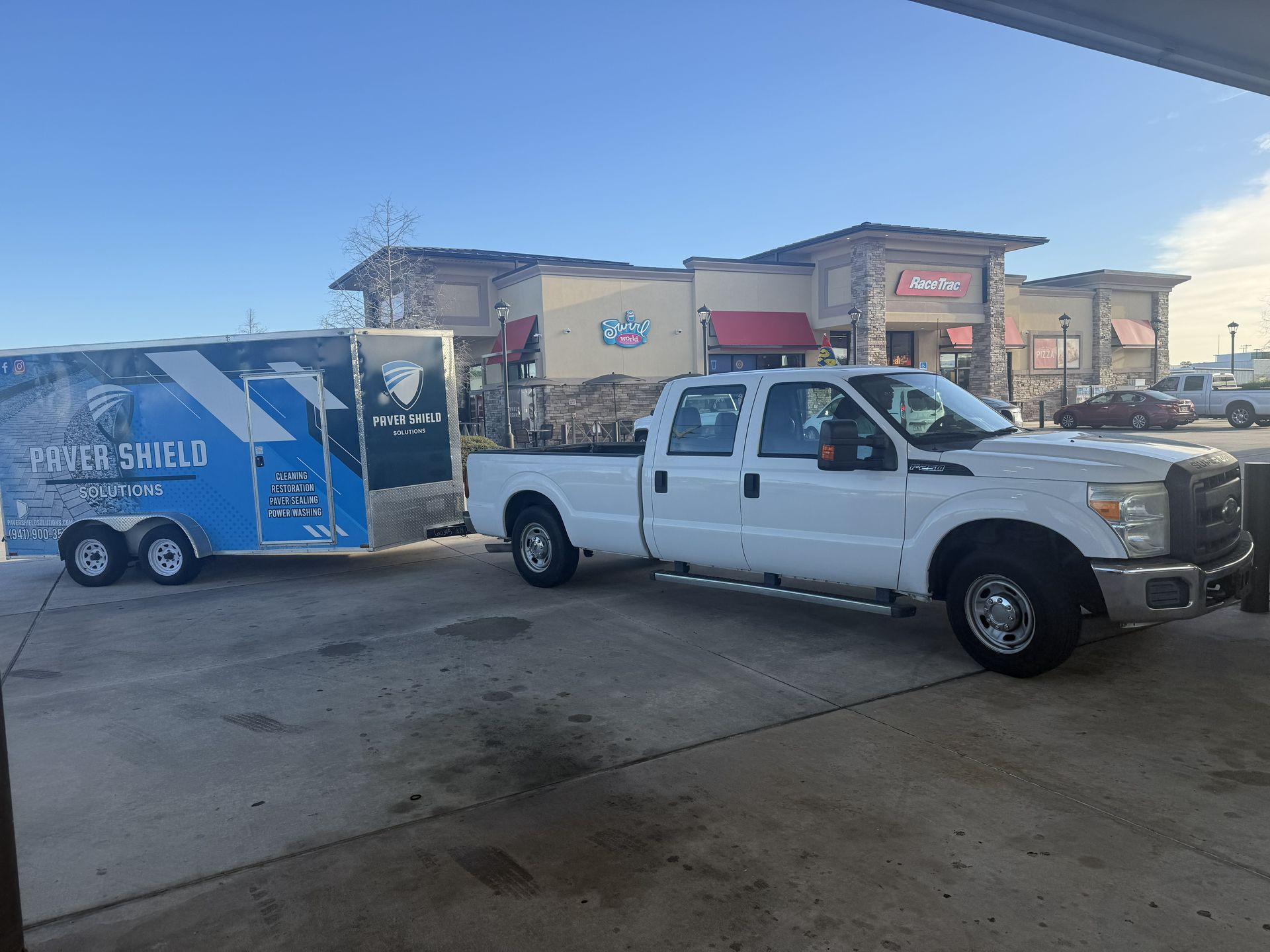 White pickup truck towing a blue Parker Shield trailer in a parking lot outside a storefront.