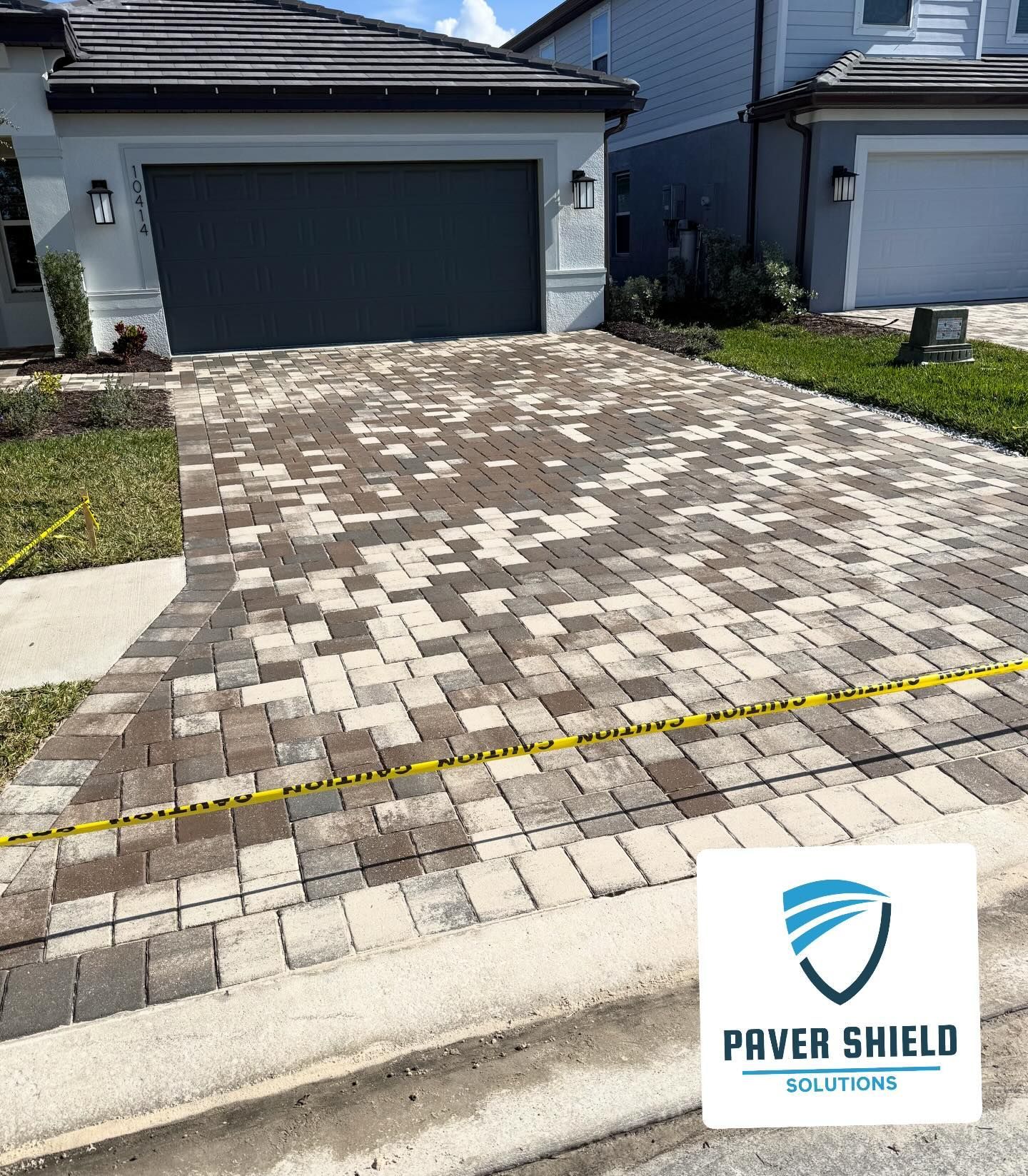 Paver driveway with patchy discoloration in front of a gray garage and house