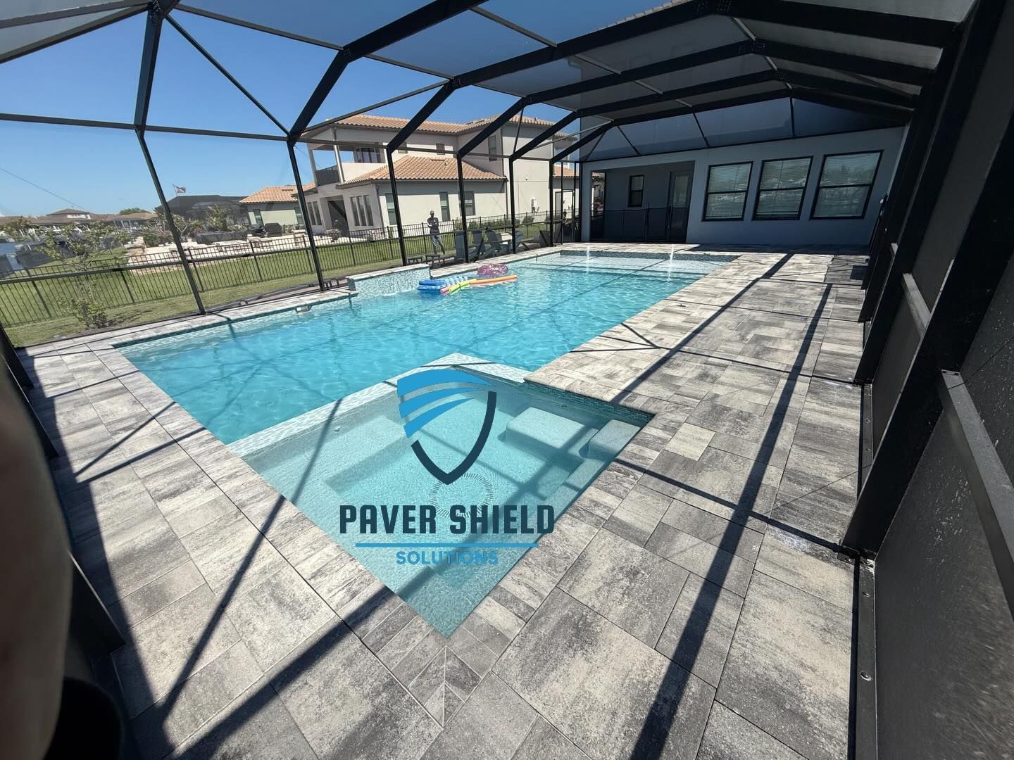 Screened backyard pool with blue water, patio pavers, and a house in the background