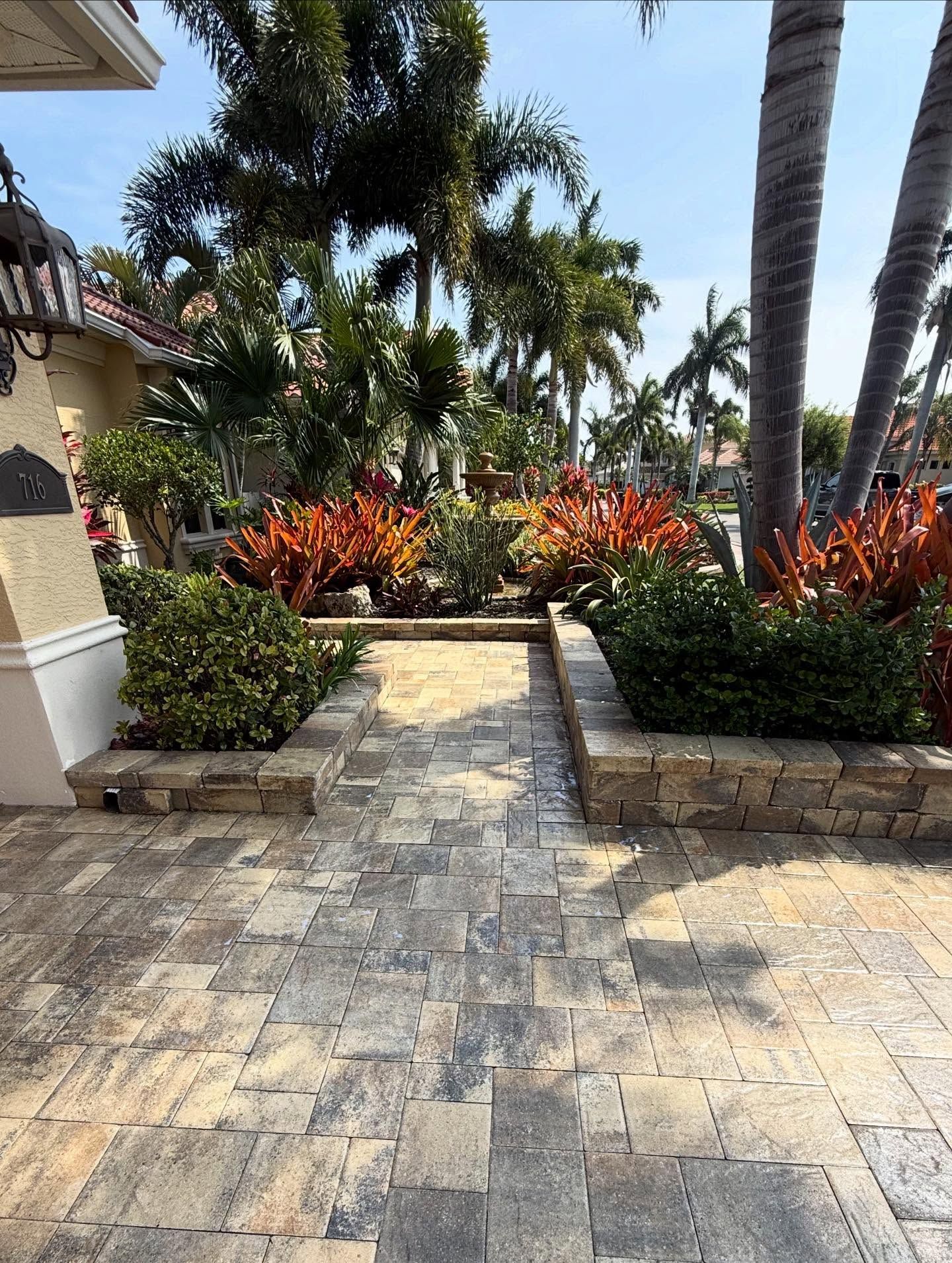 Stone walkway leading to a tropical garden with palm trees and colorful red-orange shrubs