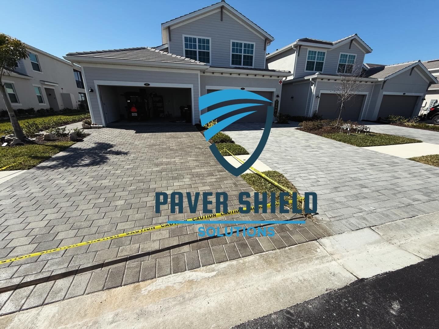 Paver Shield logo over a driveway and house exterior with gray pavers and a garage