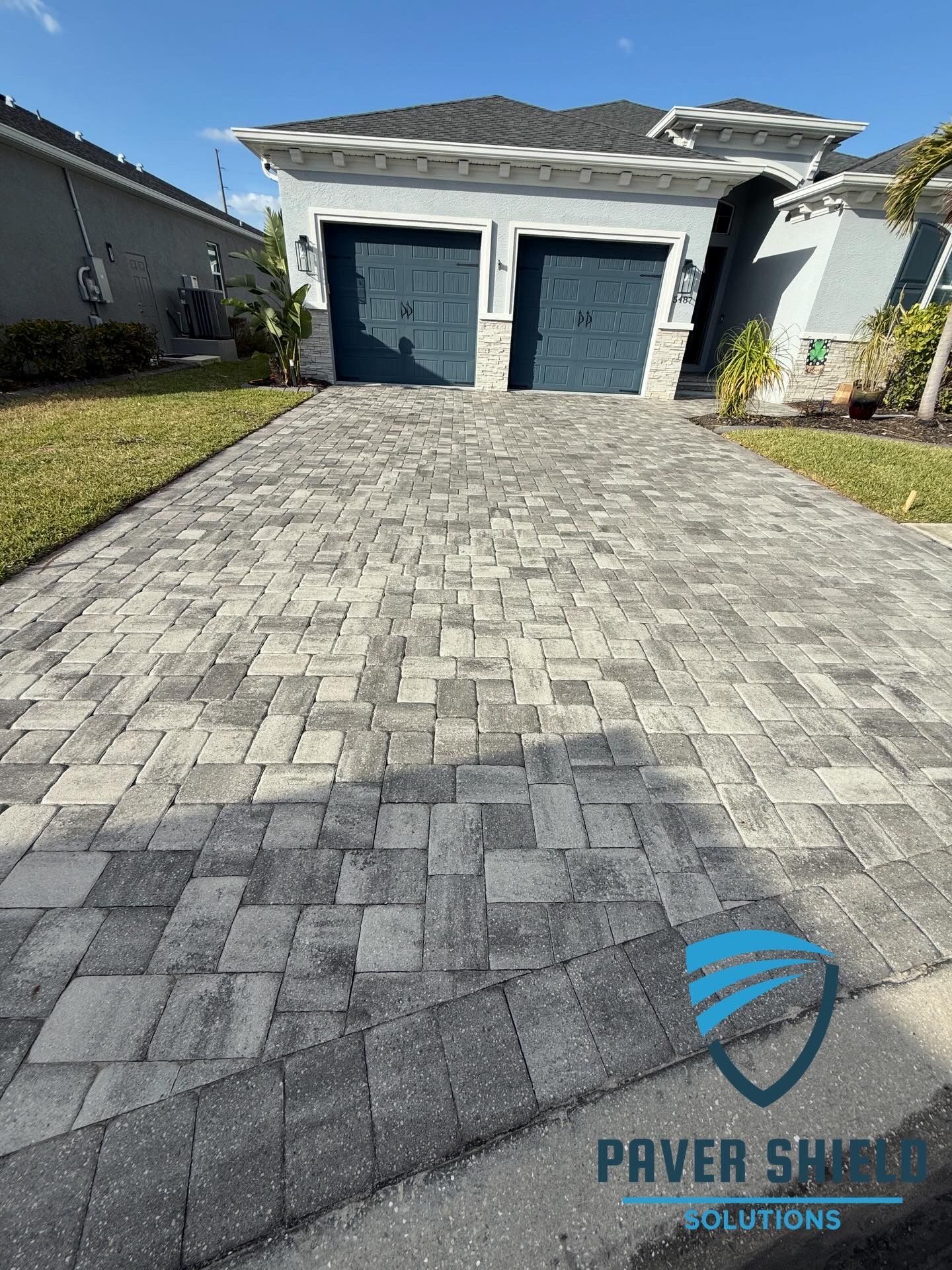 Gray paver driveway leading to a two-car garage on a sunny suburban home