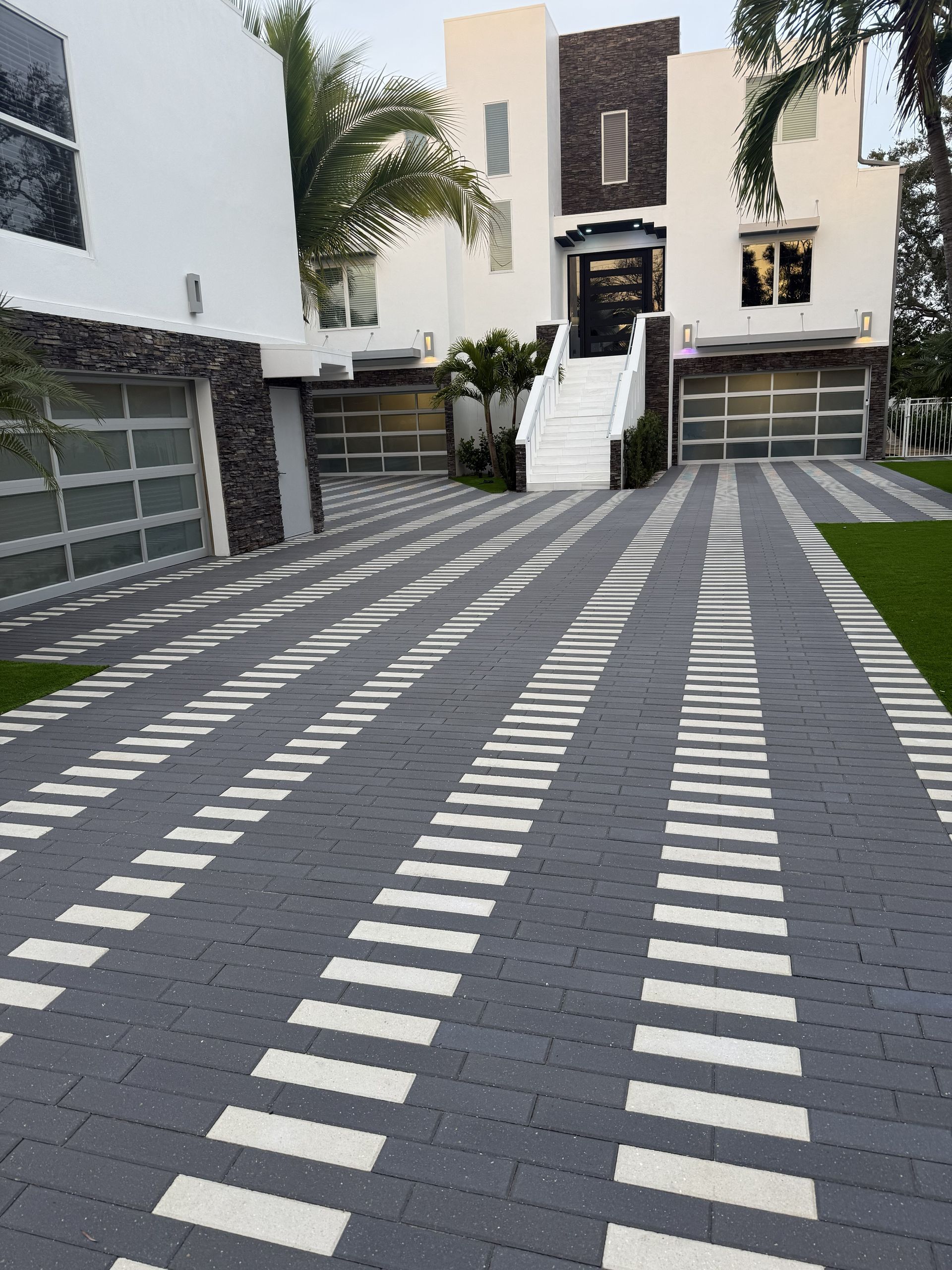 Modern house driveway with gray pavers and white striping leading to the front entrance