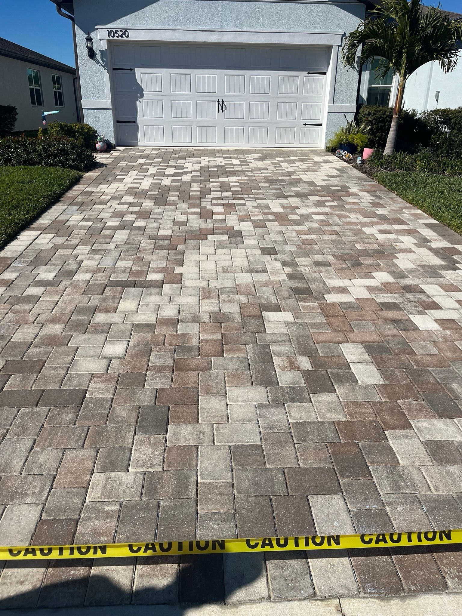 Driveway with beige pavers leading to a white garage, blocked by yellow caution tape at the bottom edge.