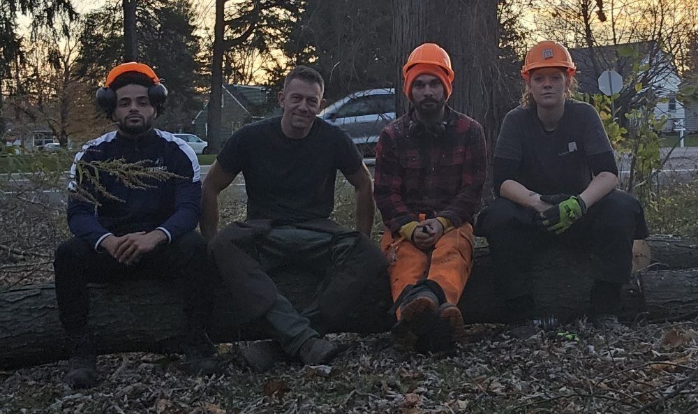 A group of men are sitting on a log in the woods.