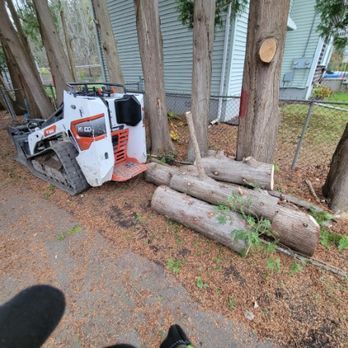 A bulldozer is sitting next to a pile of logs in front of a house.