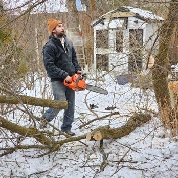 A man is cutting a tree branch with a chainsaw in the snow.