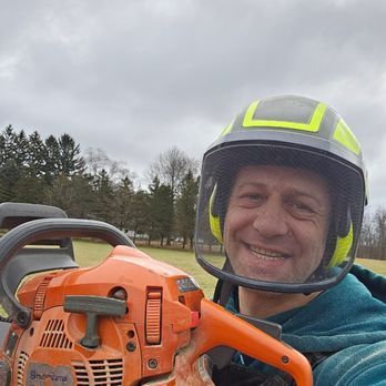 A man wearing a helmet is holding a chainsaw.