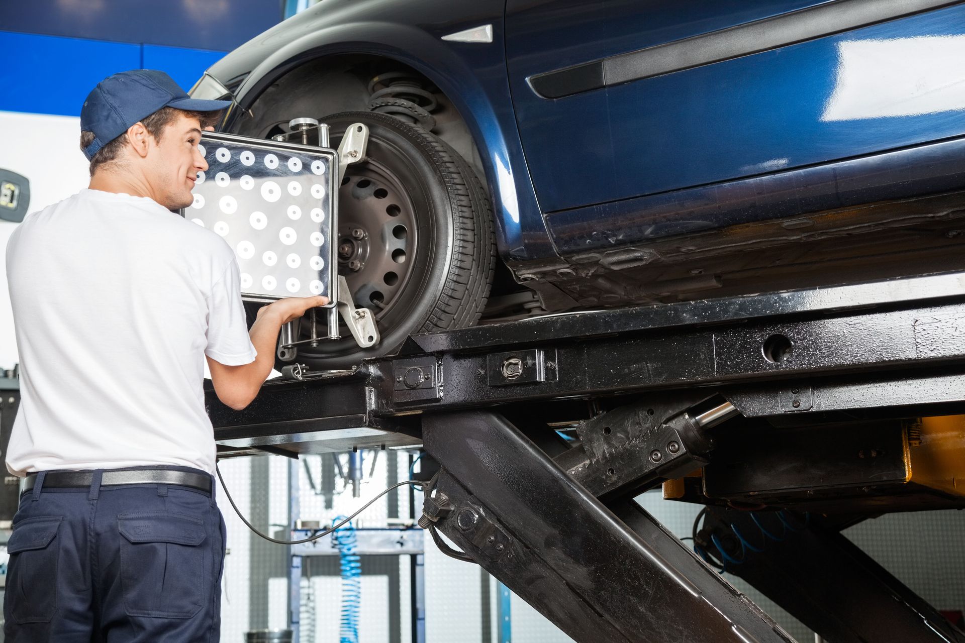 Mechanic aligning a blue car's wheel on a lift using alignment equipment in a garage.