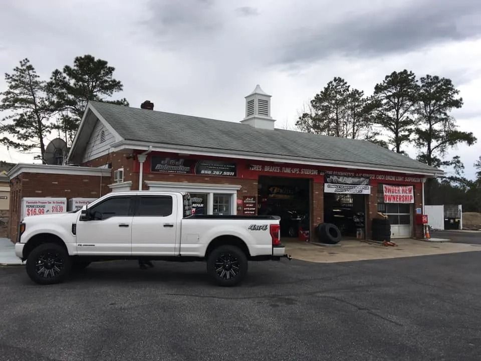 White truck parked outside a red brick auto repair shop with a cloudy sky.