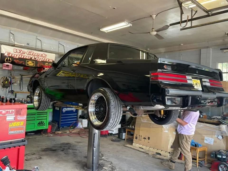 Black Buick Regal on a lift in a garage; a person is working on it.