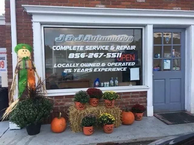 J&J Automotive shop with autumn decor, including pumpkins, flowers, and a scarecrow.