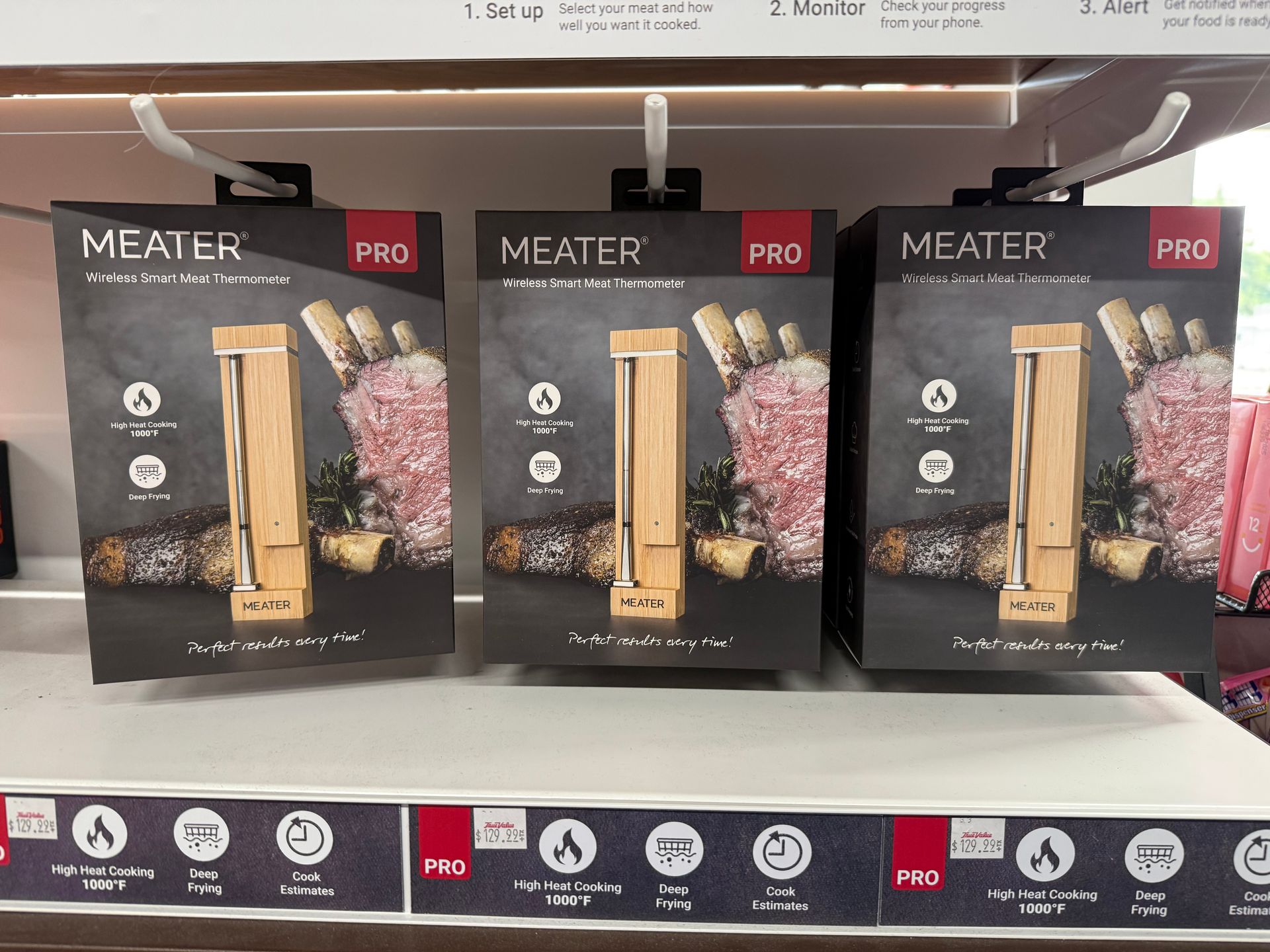 Three boxes of MEATER PRO meat thermometers displayed on a store shelf. Each box features a wooden thermometer design, and a grill background.