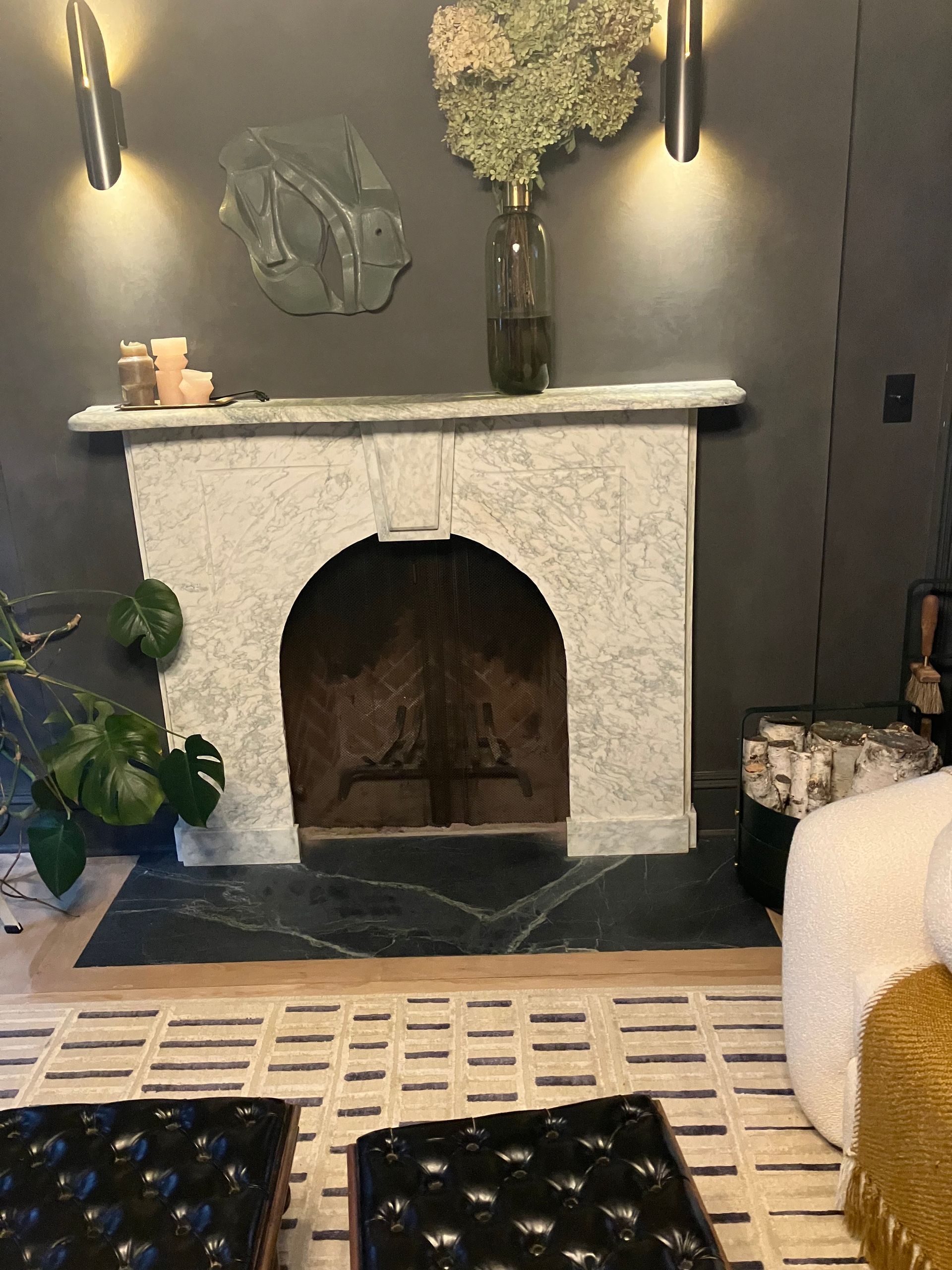 Fireplace with dried flowers and sconces, dark gray wall, and patterned floor.