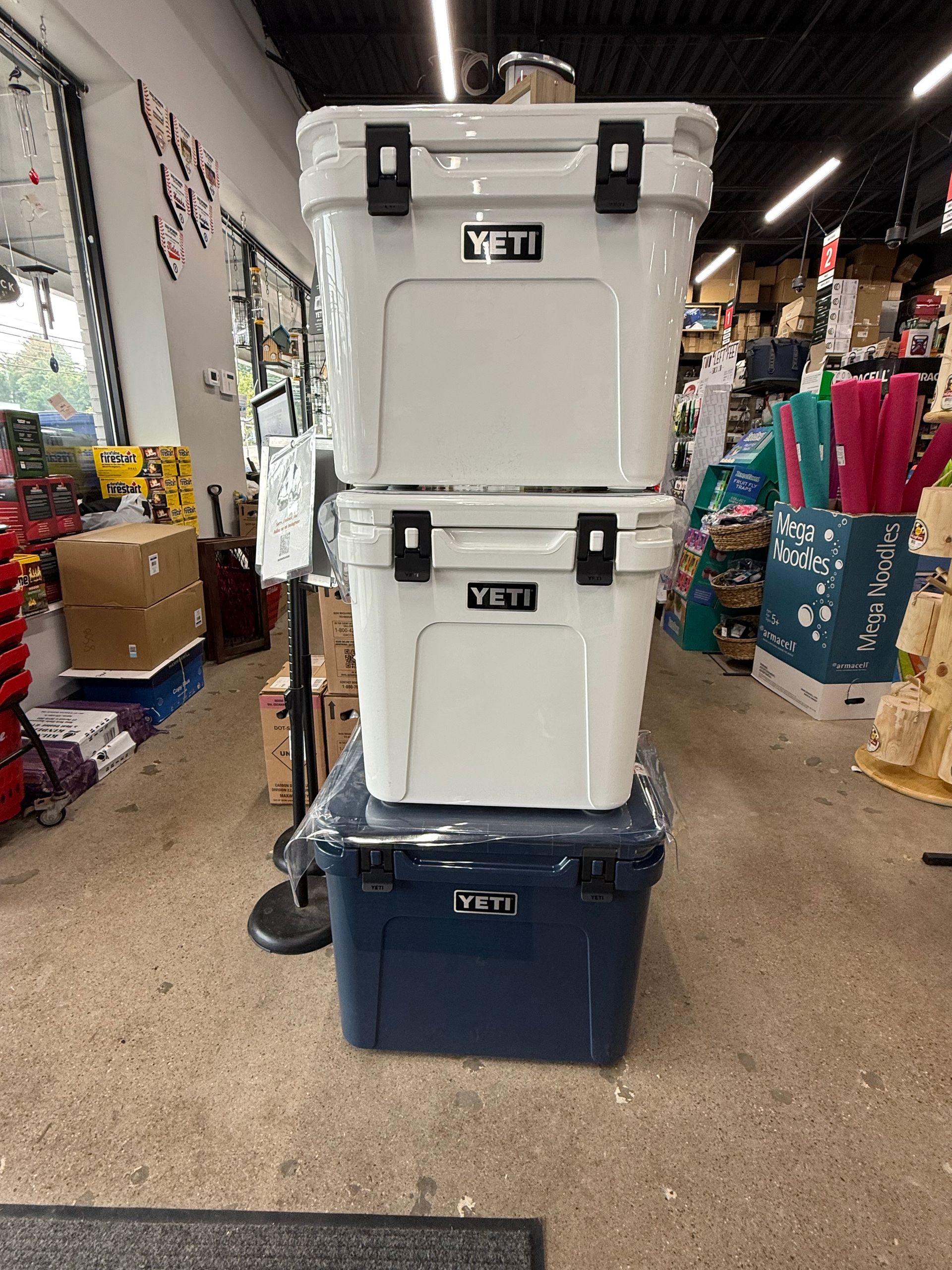 Three YETI coolers stacked: two white on top, one blue at the bottom, displayed inside a store.