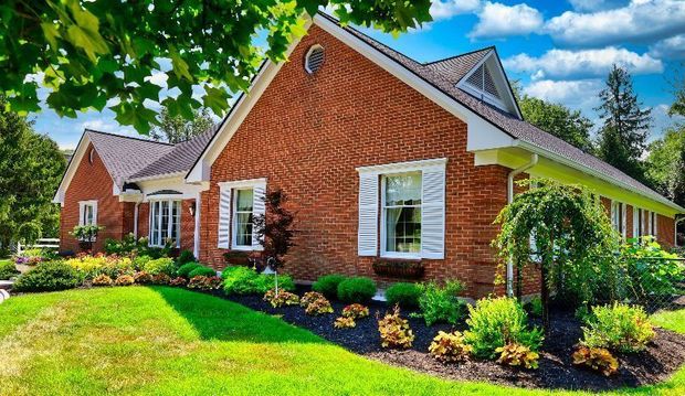 Brick house with white trim, green lawn, and garden beds.