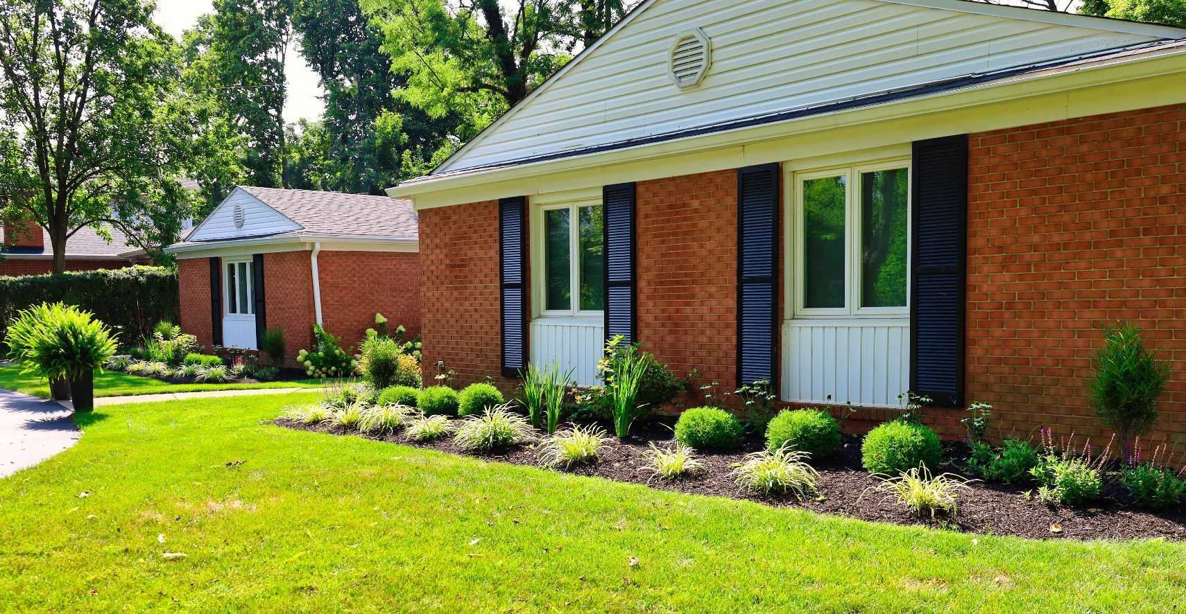 Brick ranch-style house with dark shutters, white trim, and a well-manicured lawn.