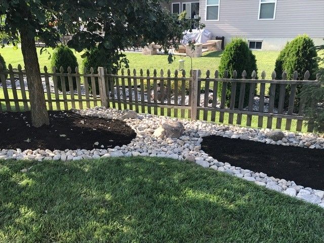 Lawn with rock border and dark mulch beds, a decorative fence, and trees.