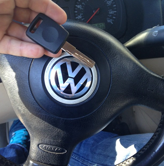 Hand holding a Volkswagen car key above a VW steering wheel
