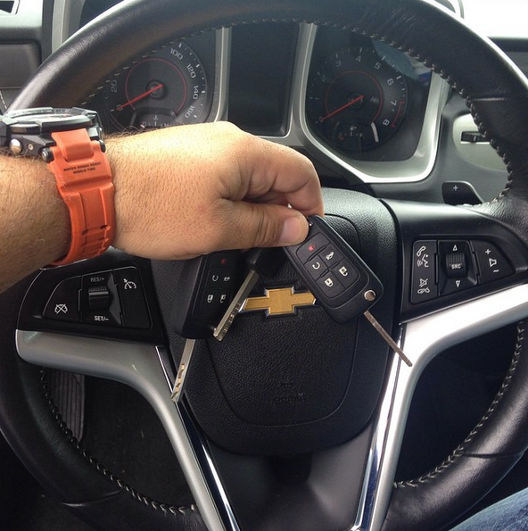 Hand holding a Chevrolet car key fob over the steering wheel and dashboard.