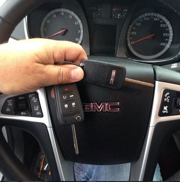 Hand holding a GMC car key fob in front of a GMC steering wheel and dashboard.