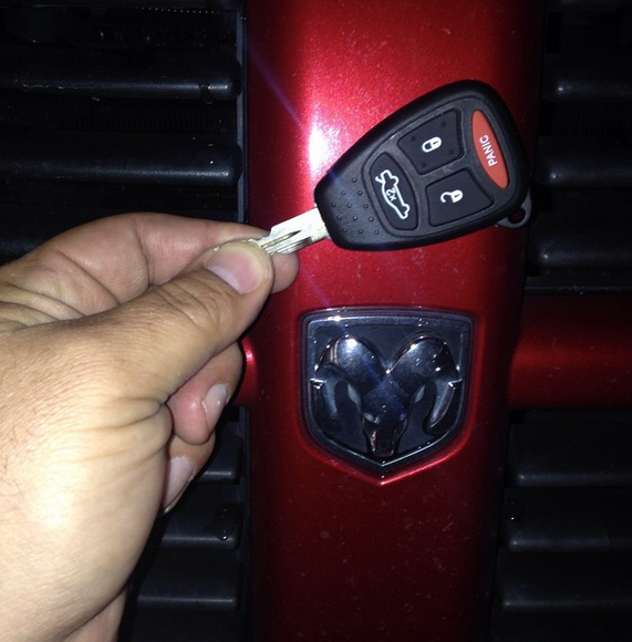 Hand holding a Dodge car key fob near a red Dodge emblem on a vehicle grille