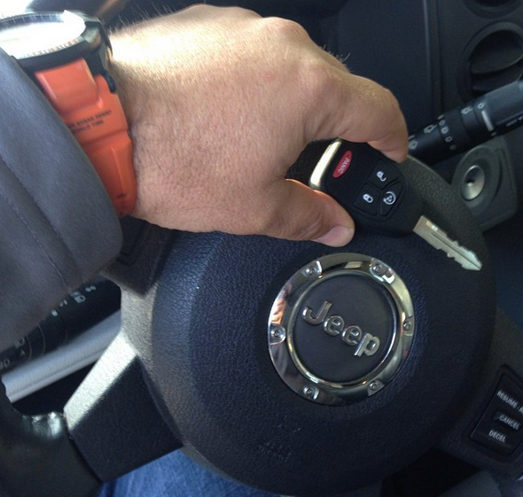 Hand holding a Jeep key fob near the steering wheel inside a car