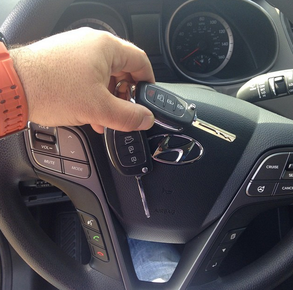 Hand holding a car key fob near a Hyundai steering wheel with dashboard controls visible