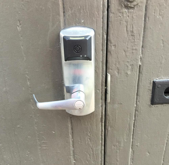 Silver electronic door lock with lever handle on a gray wooden door