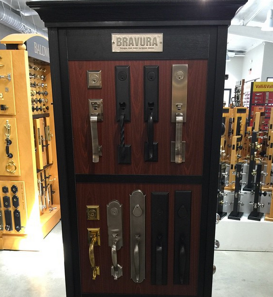 Display of decorative door handles and locks on a dark wood showroom panel in a hardware store.
