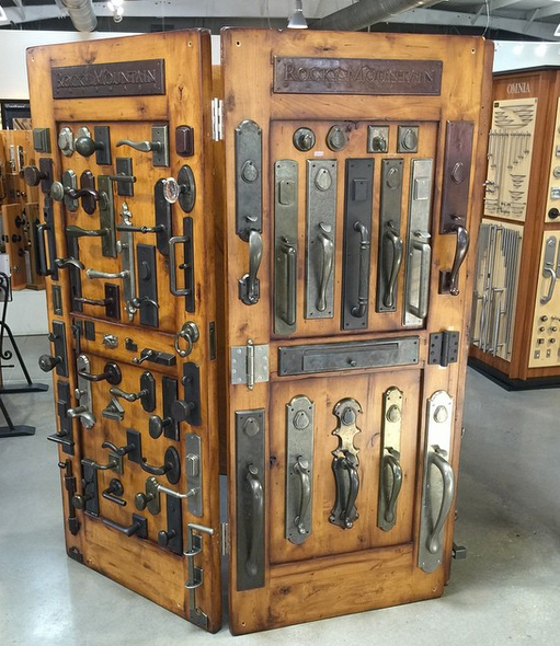 Wooden display cabinet with rows of antique metal door handles and hardware in a museum setting
