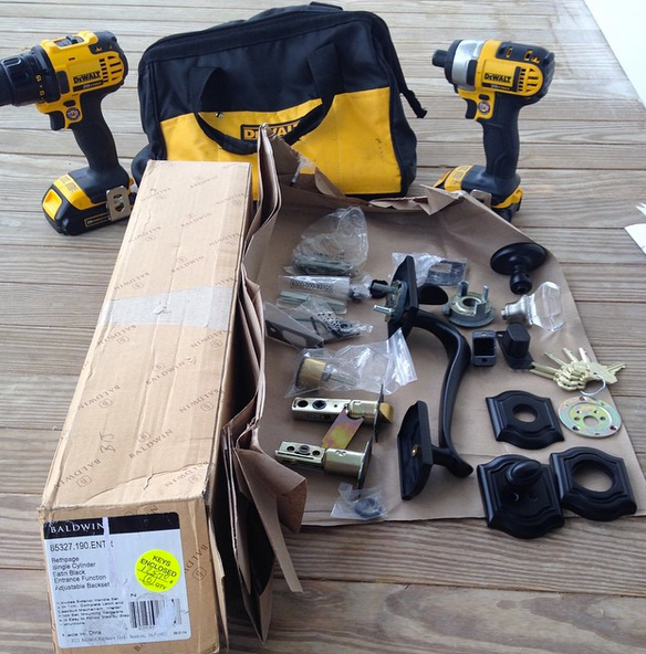 Two yellow drills, tool bag, and assorted hardware parts laid out on a wooden floor