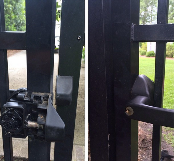 Black metal gate with a damaged latch and handle close-up, opening to a grassy yard beyond