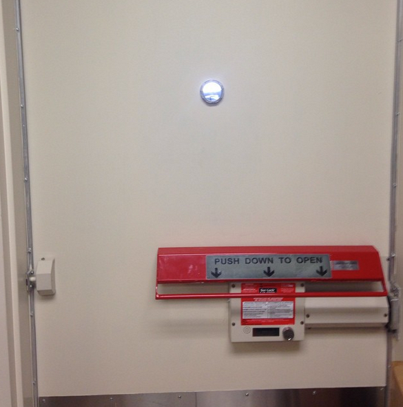 White door with red push-bar labeled “PUSH DOWN TO OPEN” and a small round window above.