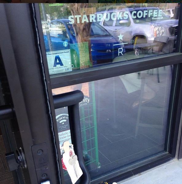 Starbucks storefront window with door handle, health grade sign, and reflections of parked cars