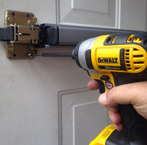 Hand holding a yellow DeWalt drill tightening a black door latch on a white paneled door
