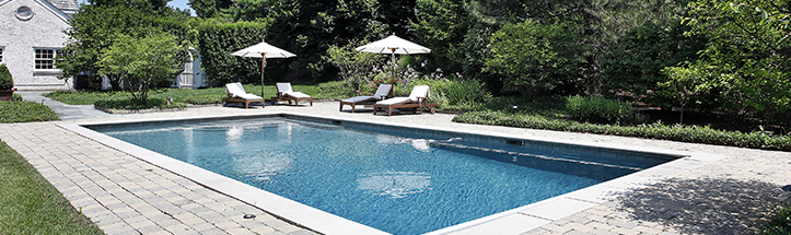 A large swimming pool with chairs and umbrellas in a backyard